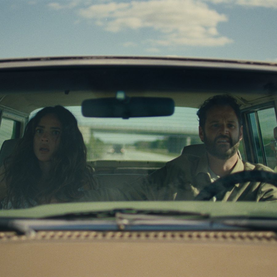 A man and woman sit in a car driving along a country road, in a scene from Splitsville.